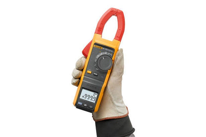 Hånd med arbejdshandske holder et Fluke 381 tangamperemeter med digitalt display.